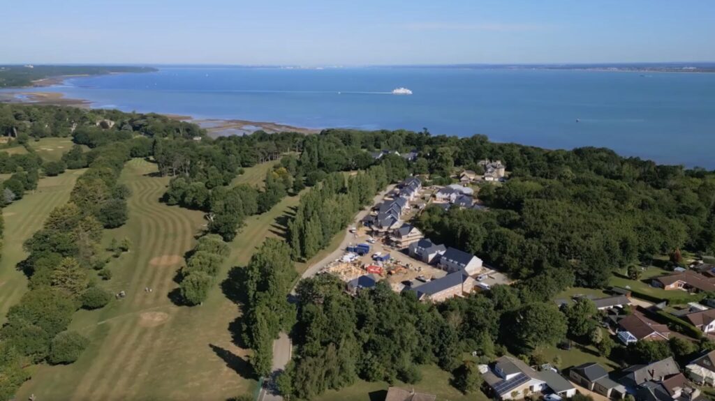 Aerial view of an Isle of Wight timber frame construction site next to a lush golf course and calm blue sea.